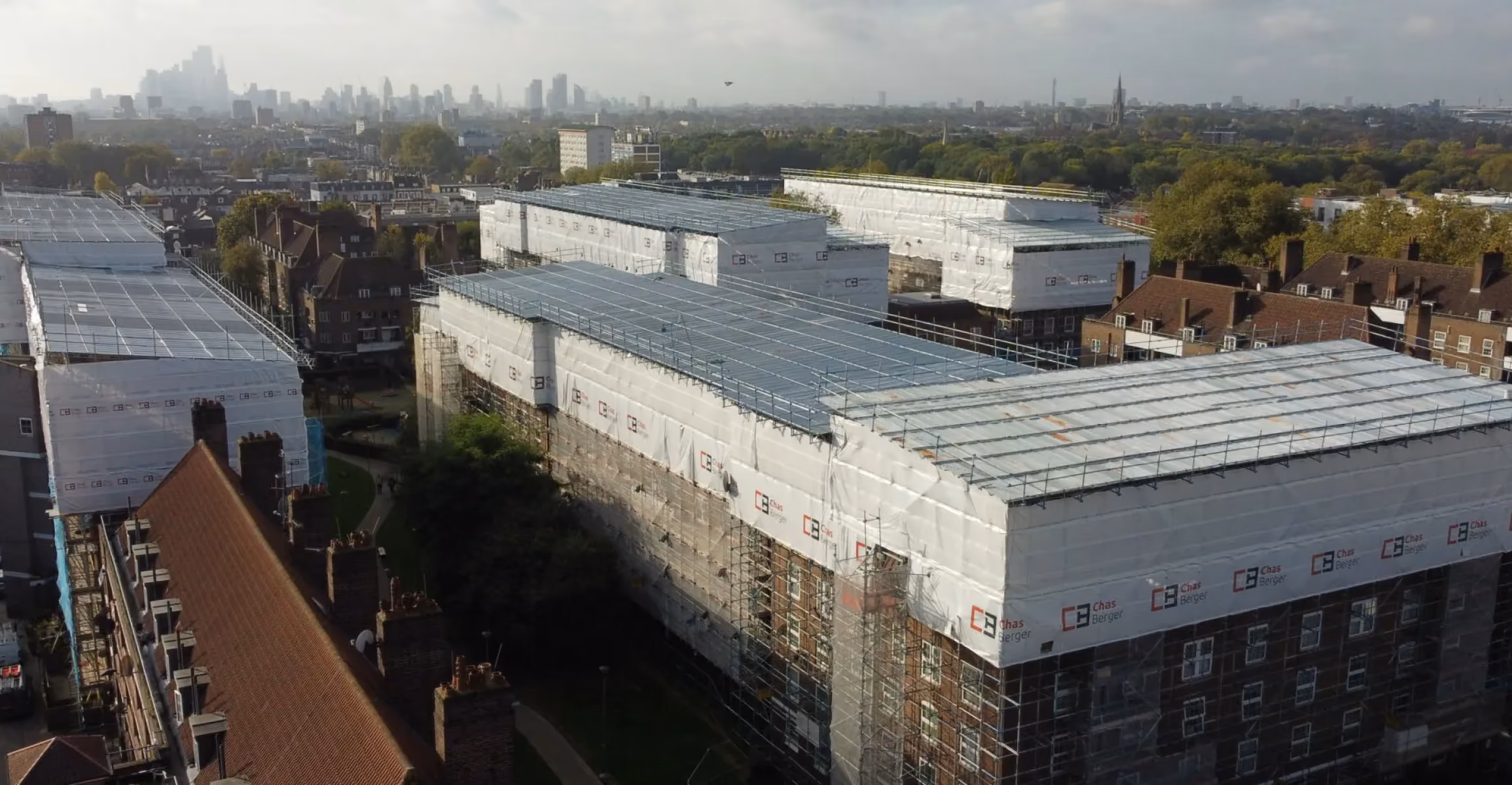 Aerial view of large buildings covered in white scaffolding wrap with solar panels on rooftops.