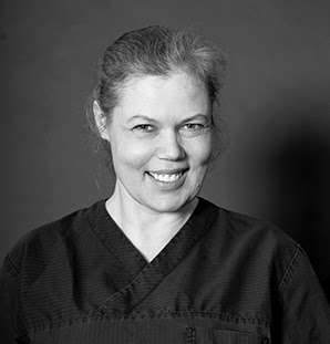 Smiling woman with tied-back hair wearing a dark top against a plain background.