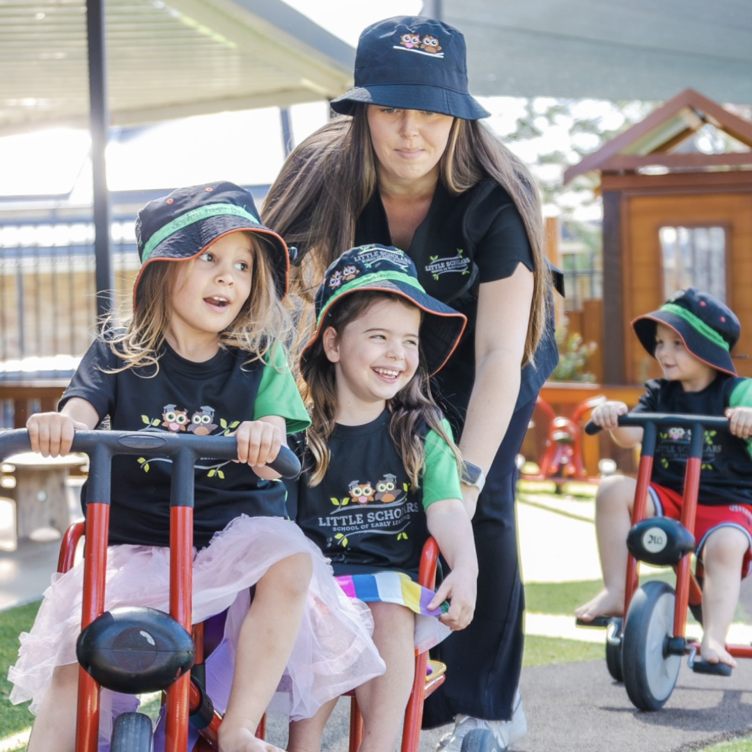 Early childhood educator helping children ride tricycles at a childcare centre
