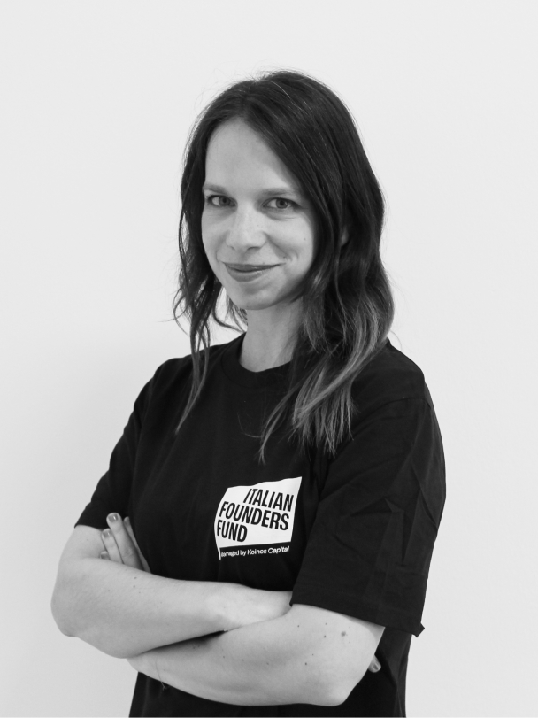 Woman with crossed arms wearing black Italian Founders Fund t-shirt, smiling against a white background.