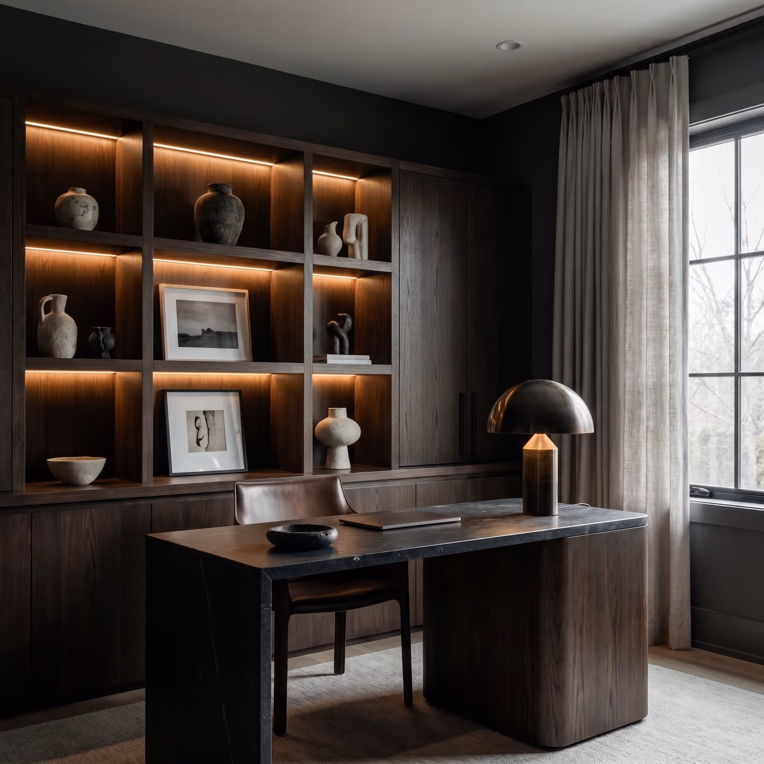 A dark wood tone desk with dark stone countertop with LED lighting custom built-ins behind it