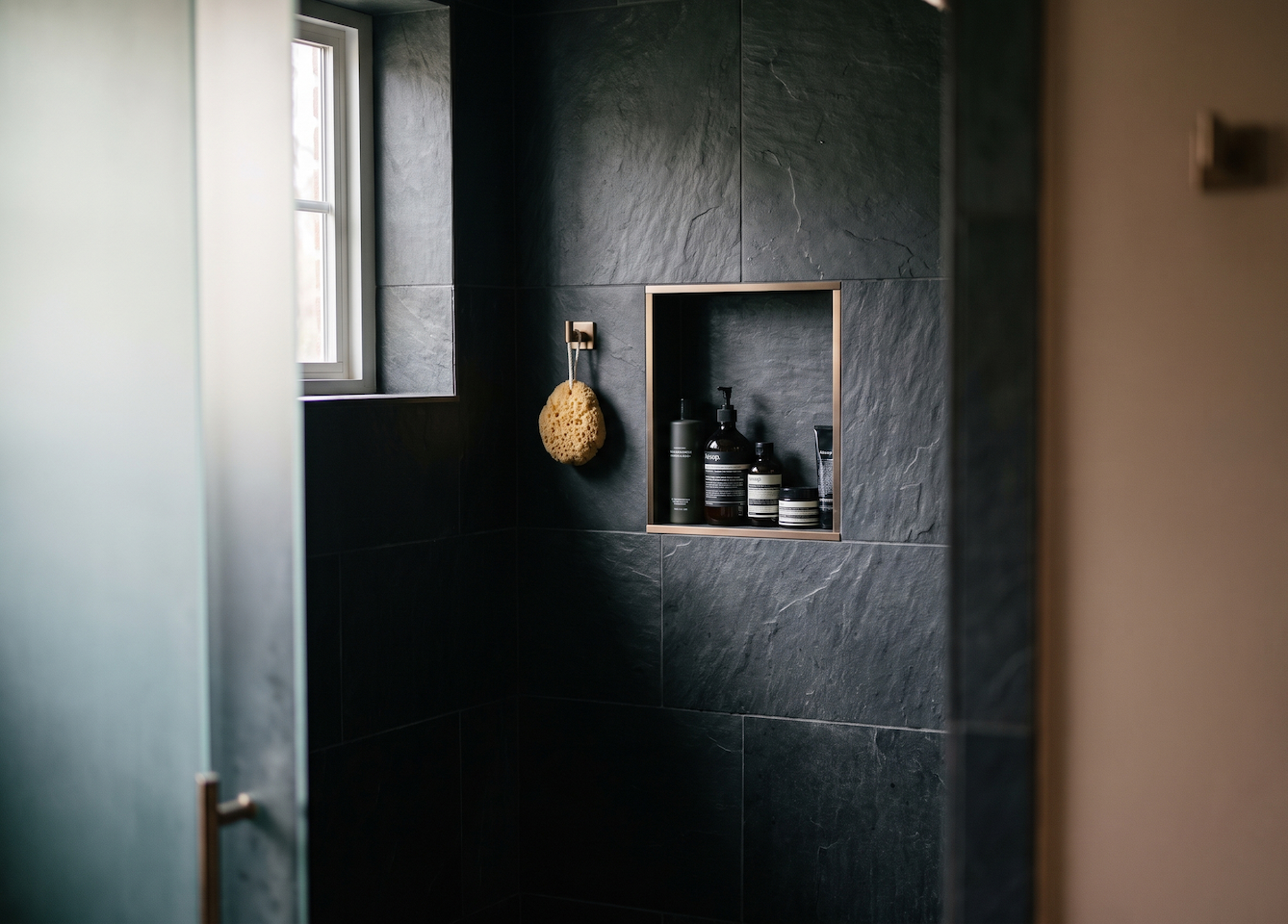 A dark tile walk-in shower with a custom niche with brass metallic accents