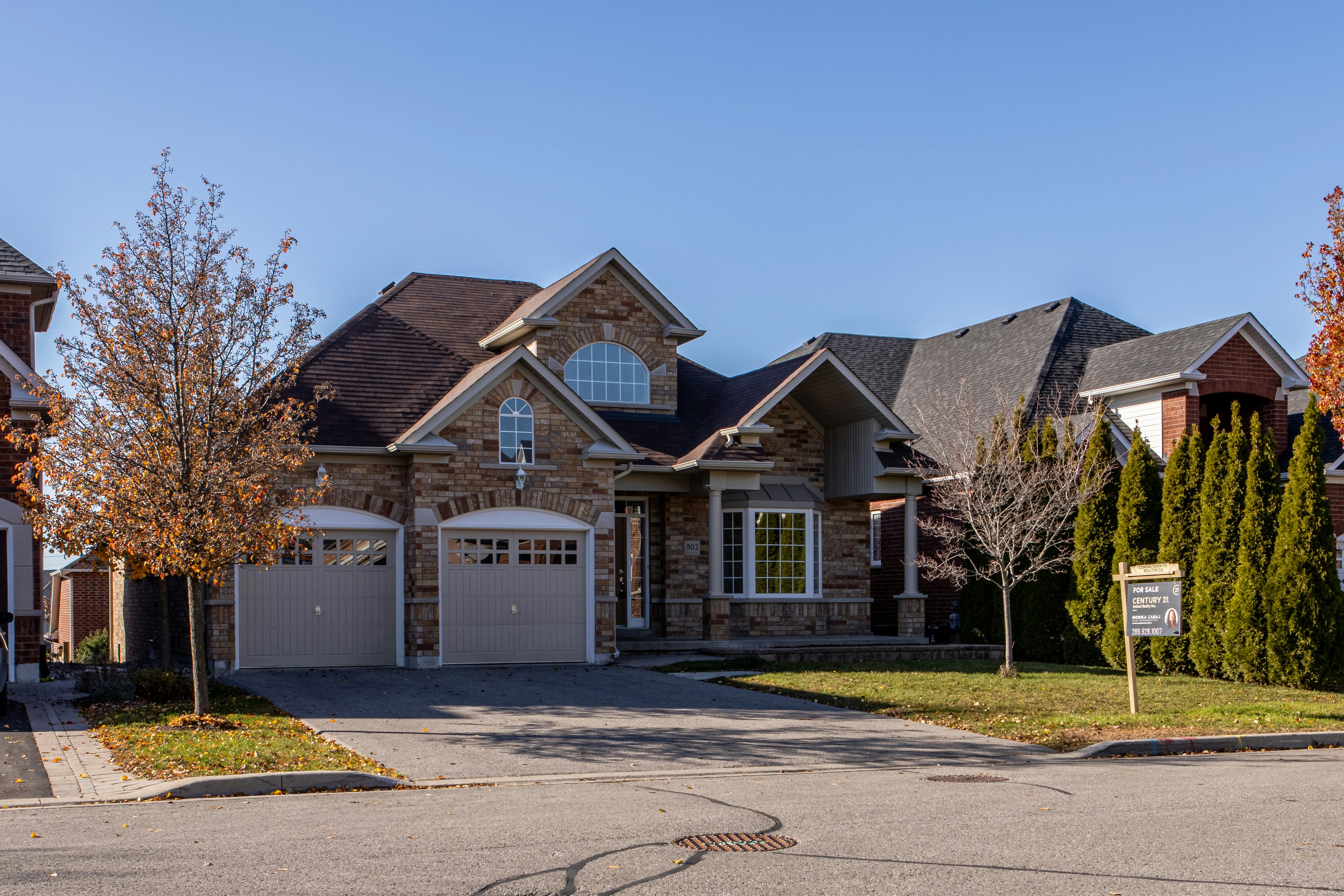 A two-storey stone and brick suburban house with an attached two-car garage and a young tree in the front yard.