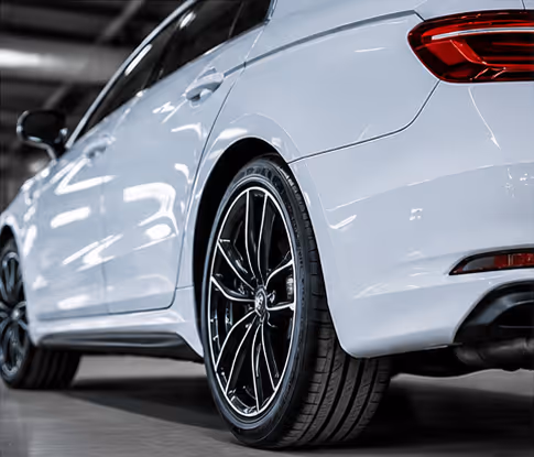 Close-up rear side view of a white modern car featuring black alloy wheels and a red tail light in an indoor parking area.