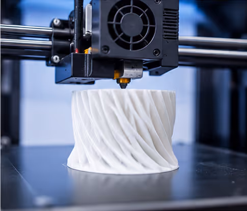 Close-up of a 3D printer head printing a white, cylindrical object with a twisted, wavy pattern on its surface.