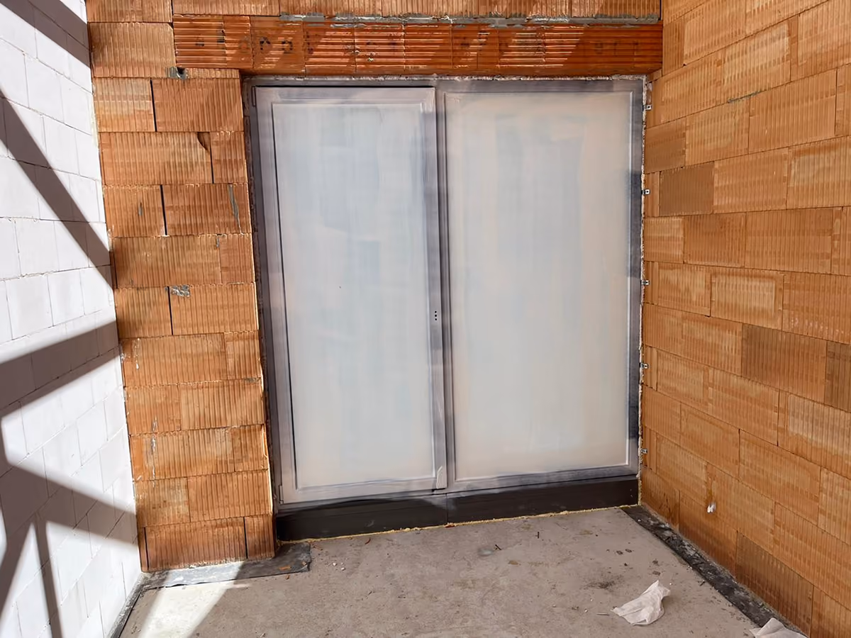 Double sliding glass door covered with peelable coating framed by unfinished brown brick walls.