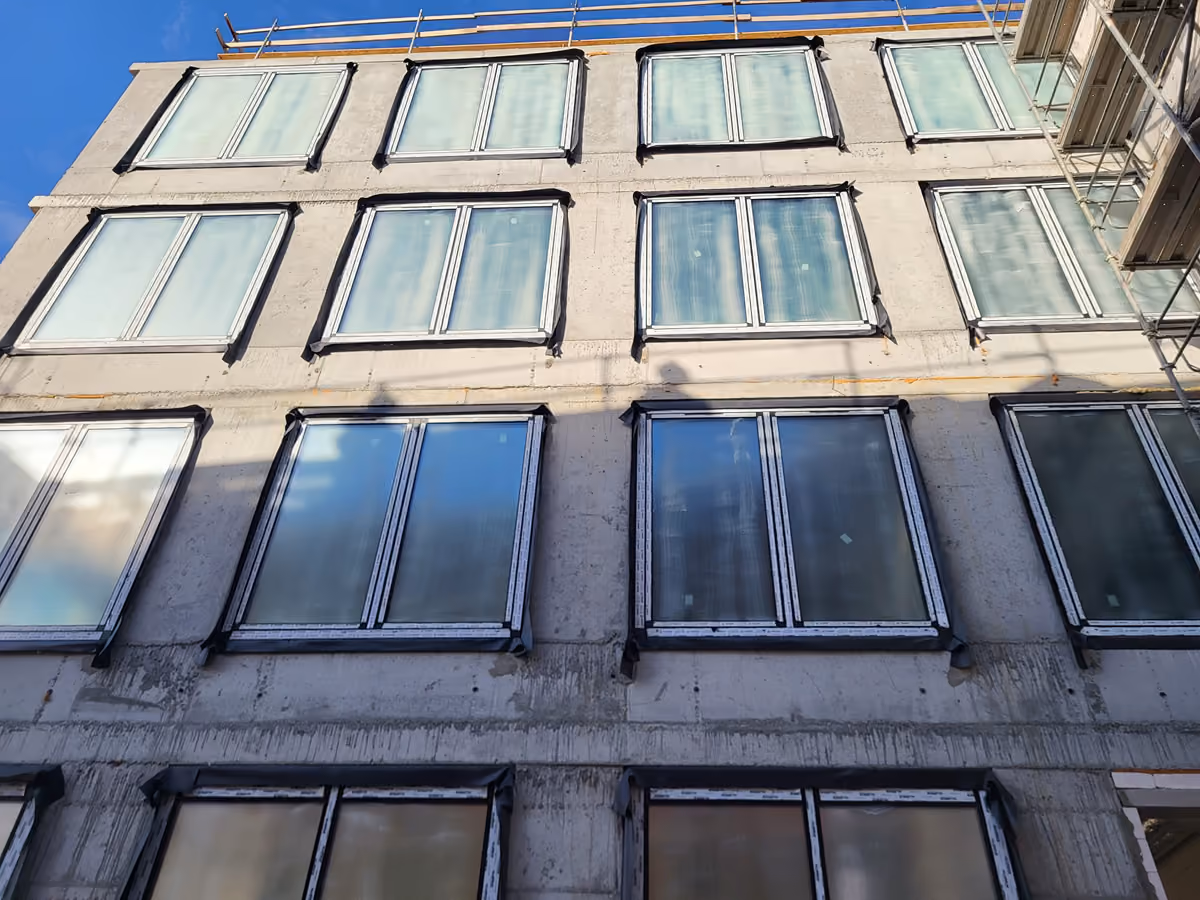 Exterior view looking up at a building facade with multiple large glass windows under construction.