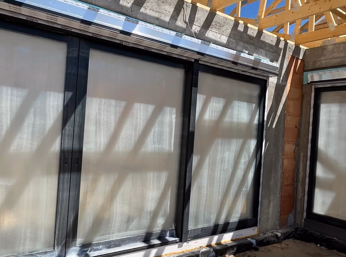 Construction site showing large black-framed windows installed in a concrete and wood frame structure.