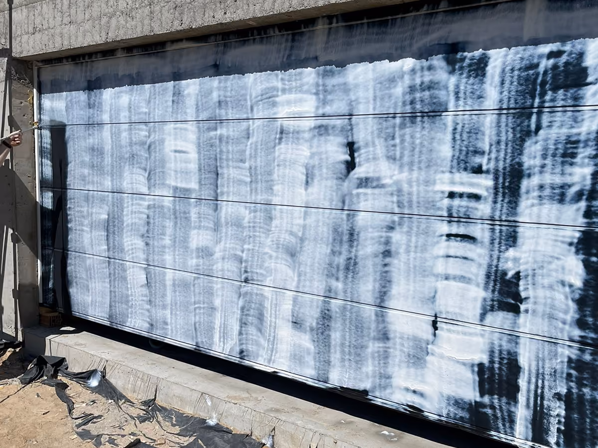 Person pressure washing a large dark garage door with white protective coating streaks.