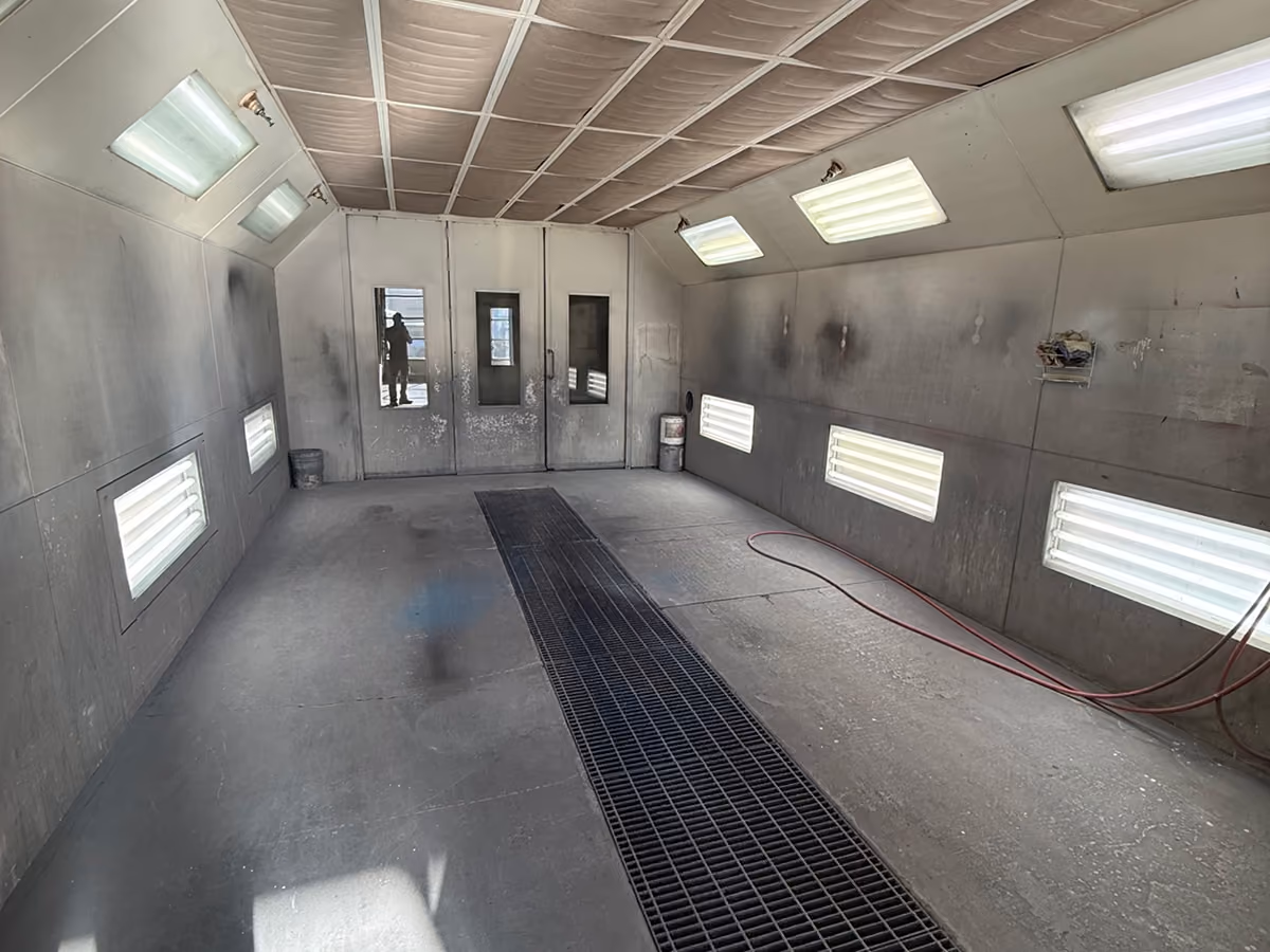 Empty industrial spray booth with grated floor vent, lit ceiling and side lights, and double doors at the end.