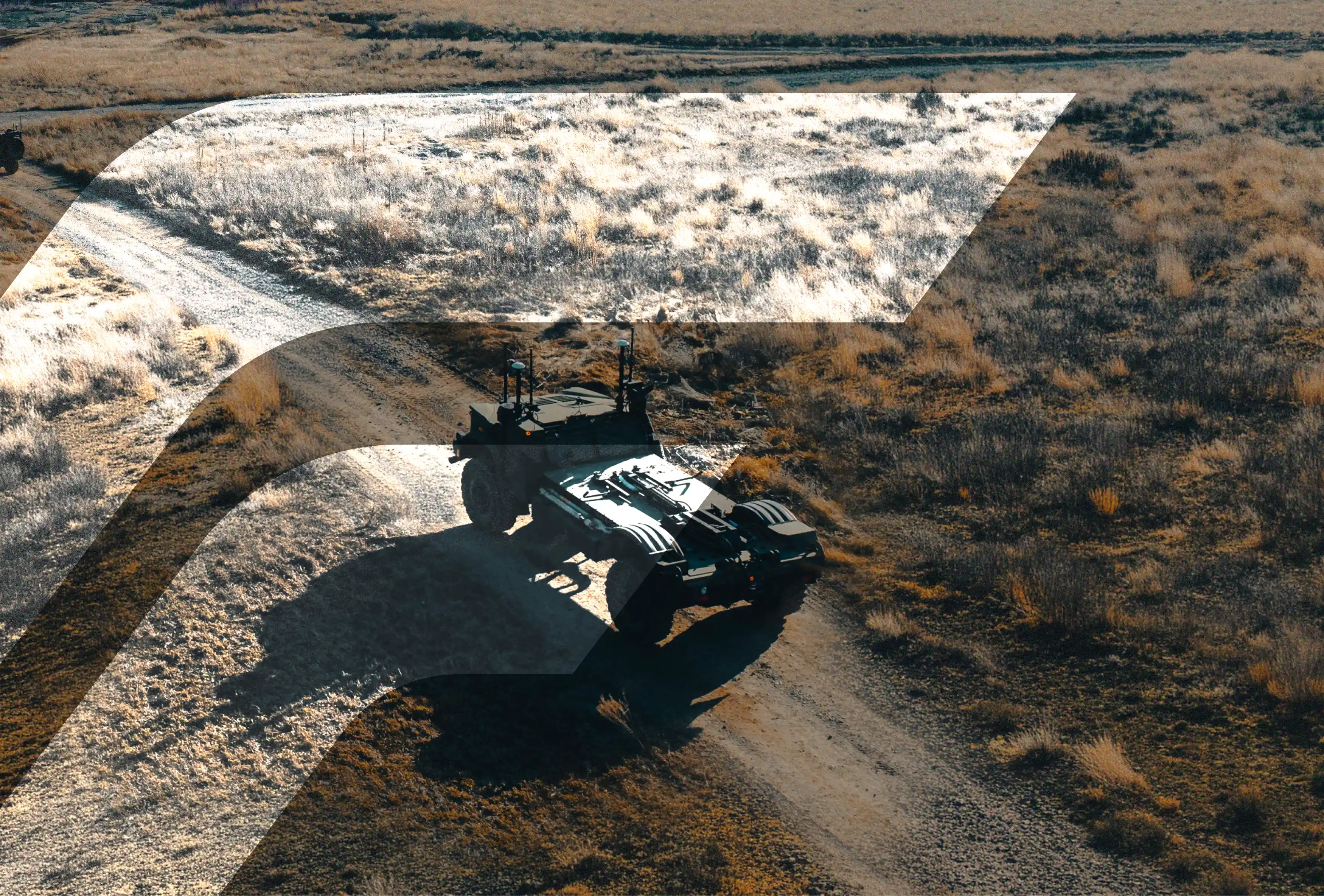 Military unmanned vehicle driving on a dirt road in a dry grassy field with shadows.