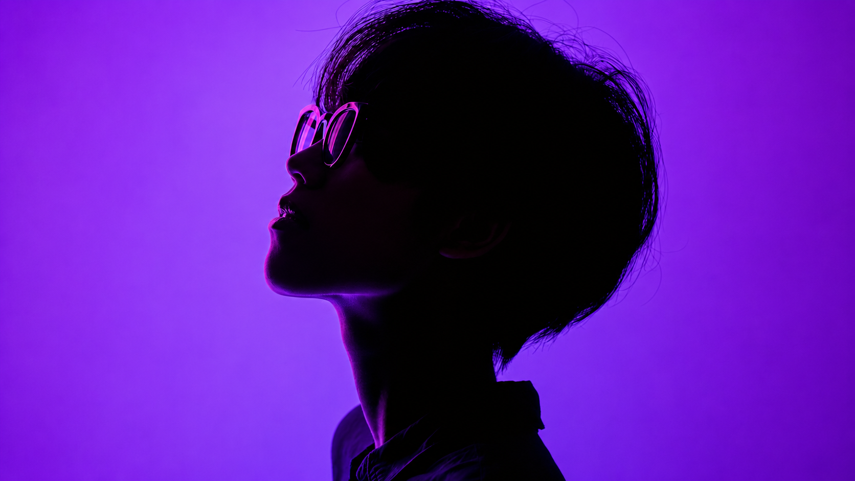 Silhouette of a person wearing glasses against purple background with neon light accents.