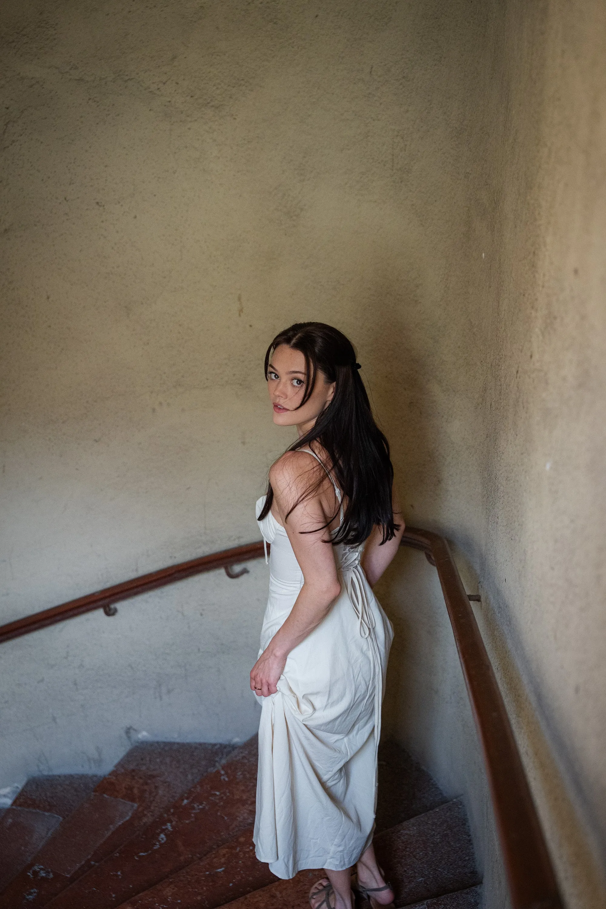 Model Julia in a white dress on a sunlit stairwell, In White editorial by GROOVE Media