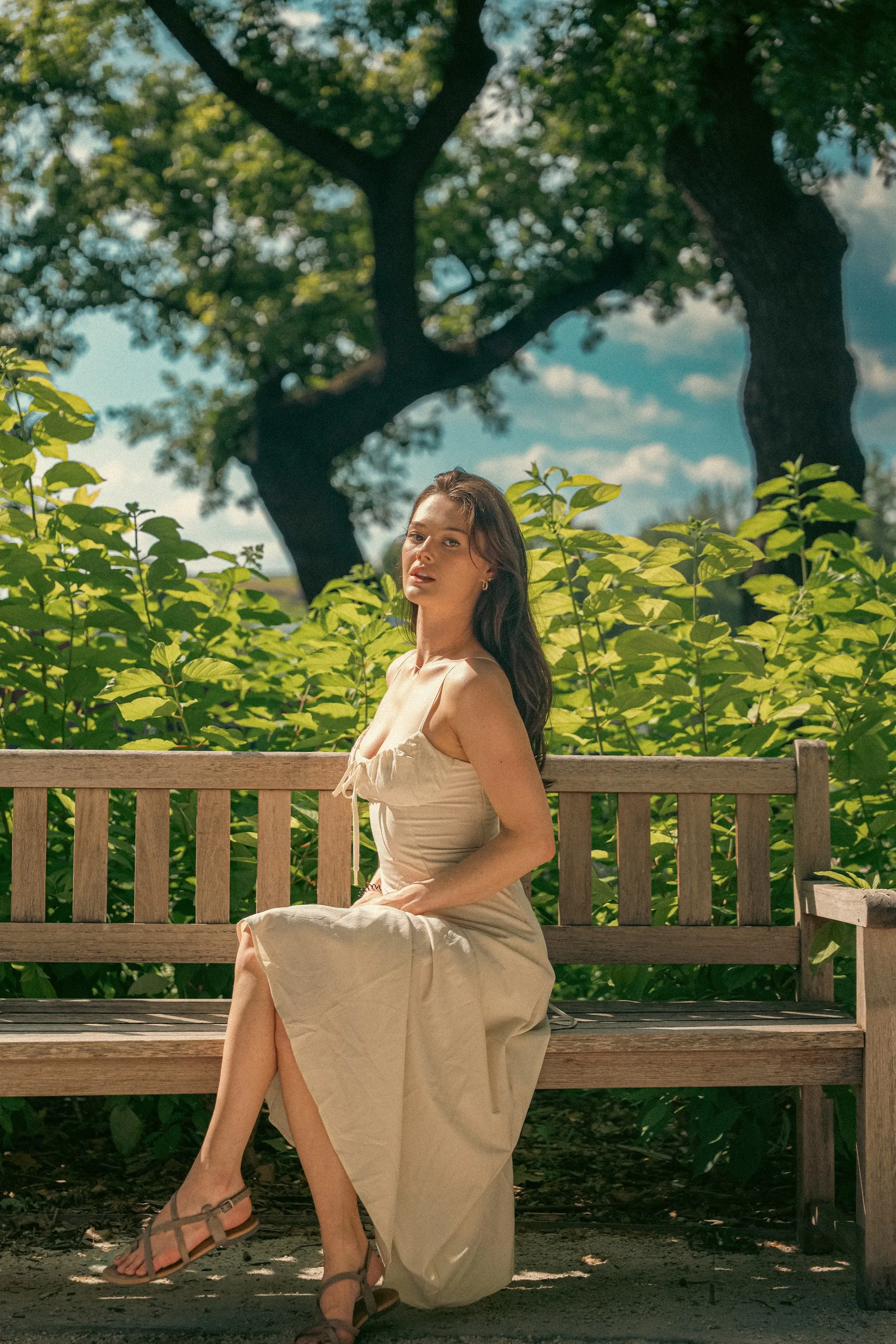 Model Julia seated on a park bench in a flowing dress, In White editorial by GROOVE Media
