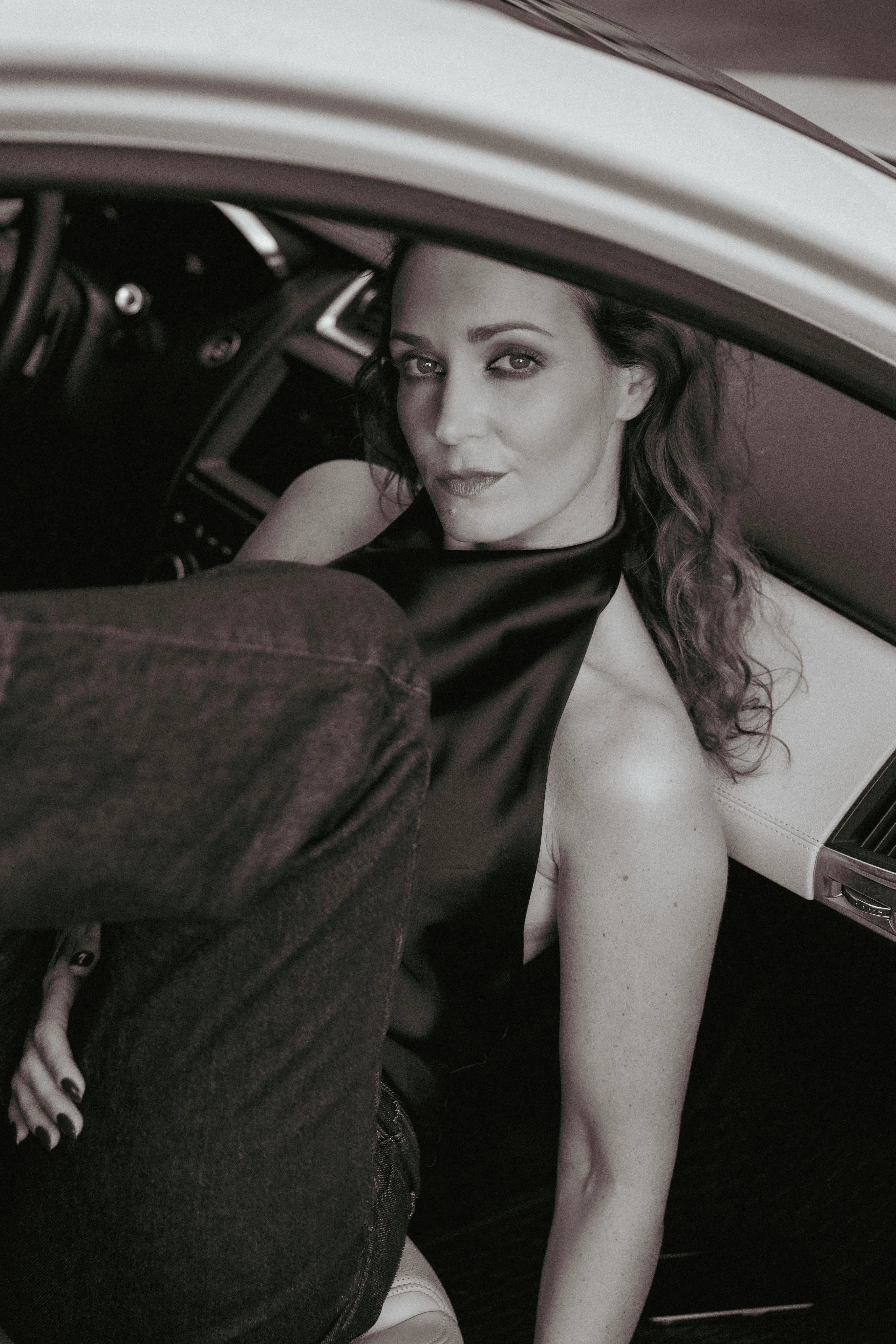 Kinga seated in an open car door, black-and-white portrait by GROOVE Media