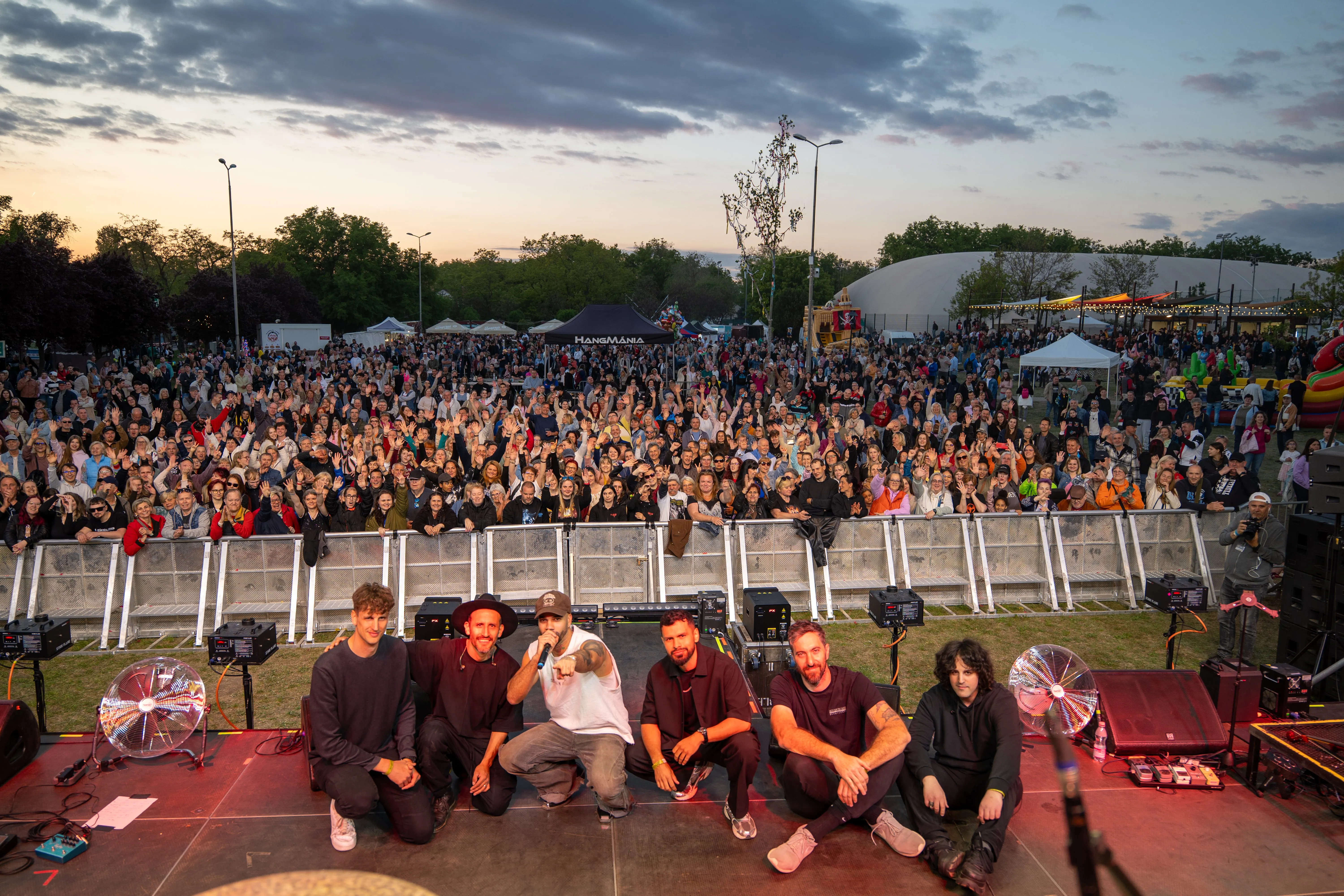 A band posing on stage in front of a packed festival crowd at dusk, concert photography by GROOVE Media