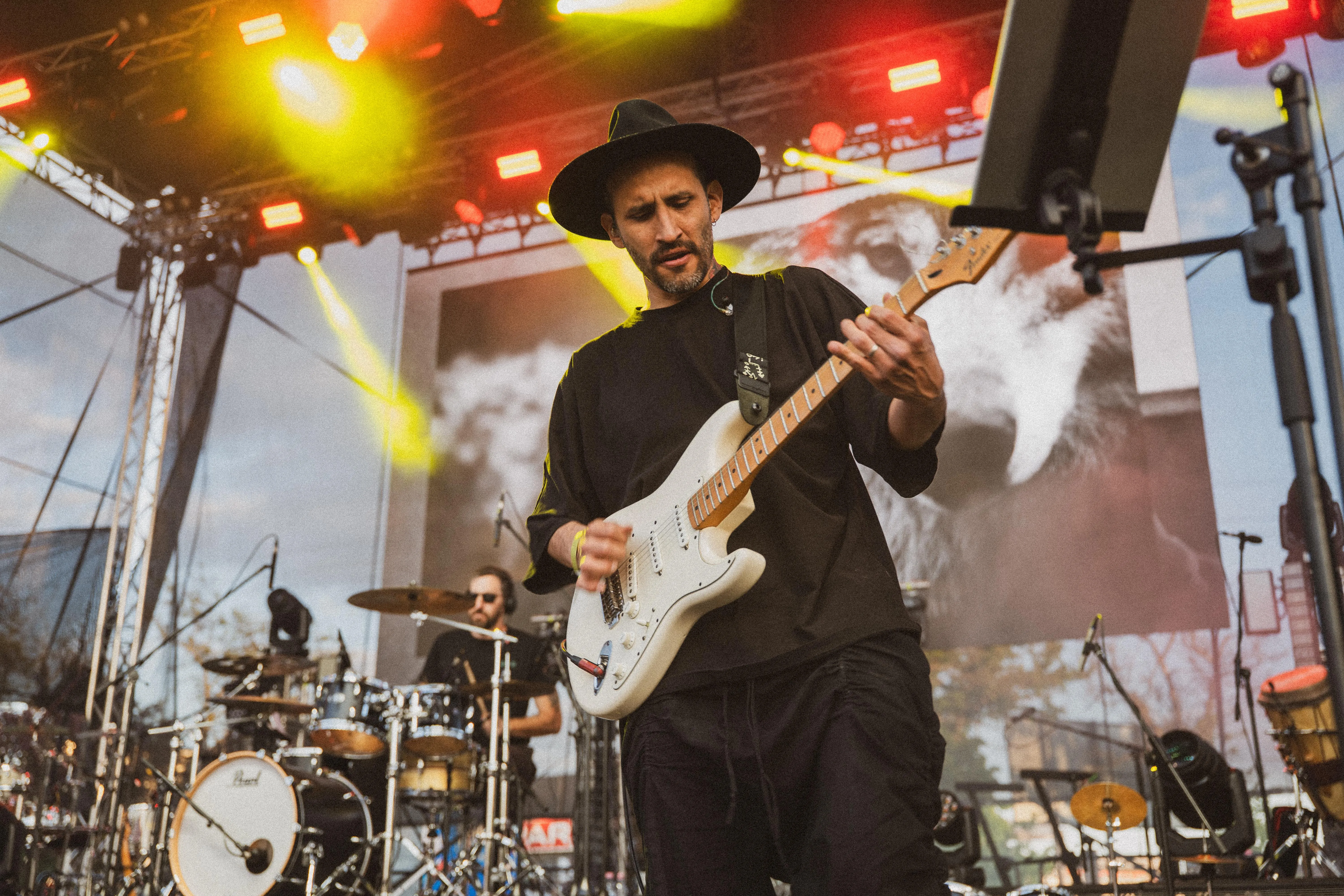 Guitarist in a wide-brimmed hat playing under festival stage lights, concert photography by GROOVE Media