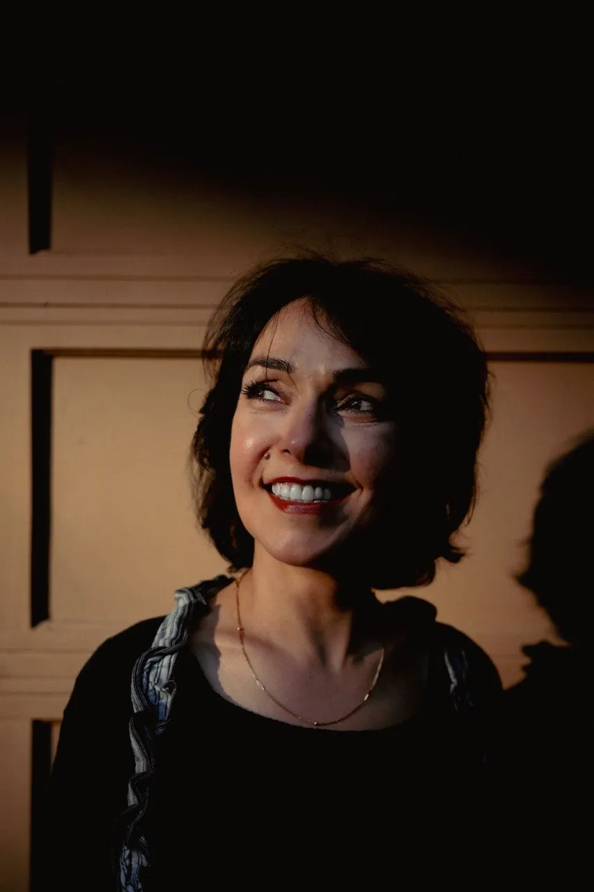 Portrait of a smiling woman in low, warm sunlight against a wooden door, by GROOVE Media