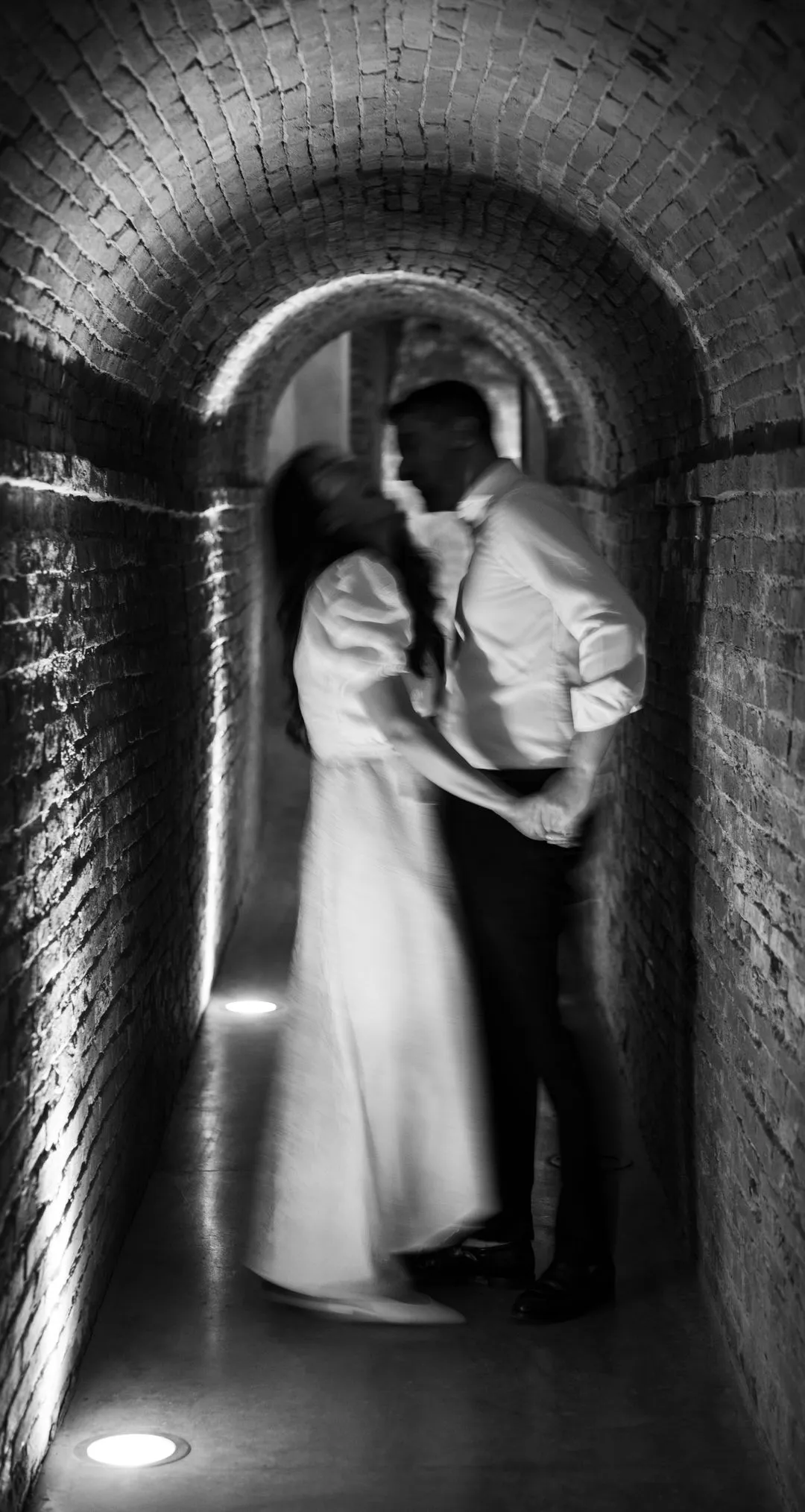 Couple dancing in an uplit brick tunnel with motion blur, black and white wedding photography by GROOVE Media