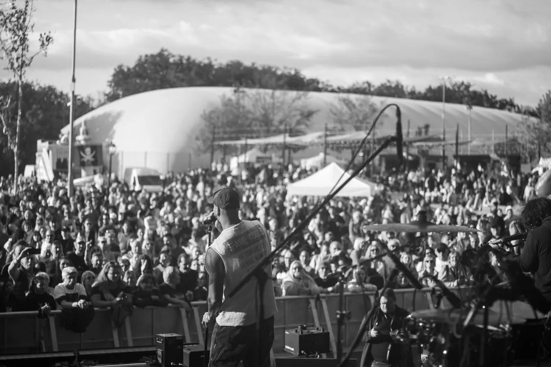 Singer on an outdoor festival stage facing a huge crowd, black and white concert photography by GROOVE Media