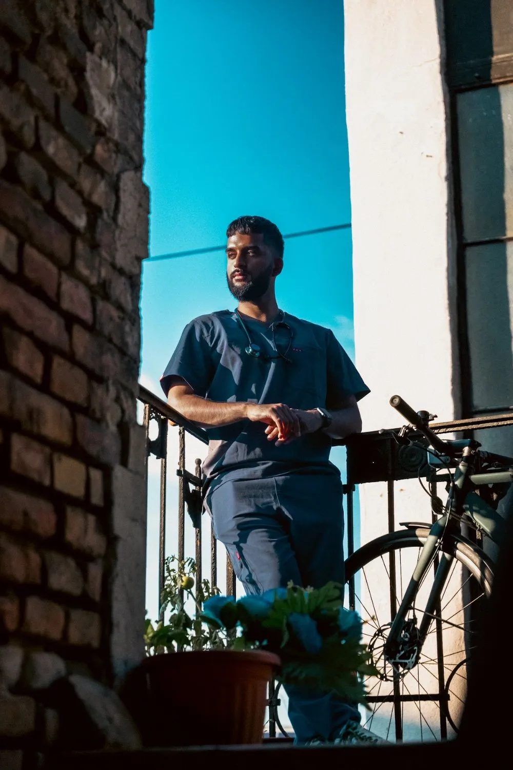 Zoubi in PAX Scrubs on a balcony beside a bicycle under a blue sky, PAX Scrubs campaign