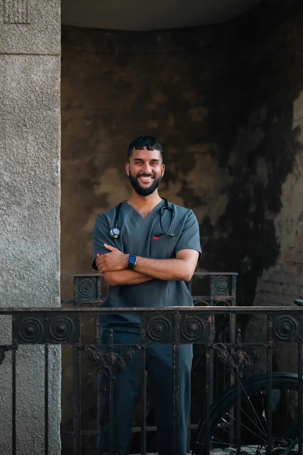 Zoubi in PAX Scrubs with arms crossed on a courtyard balcony, PAX Scrubs campaign