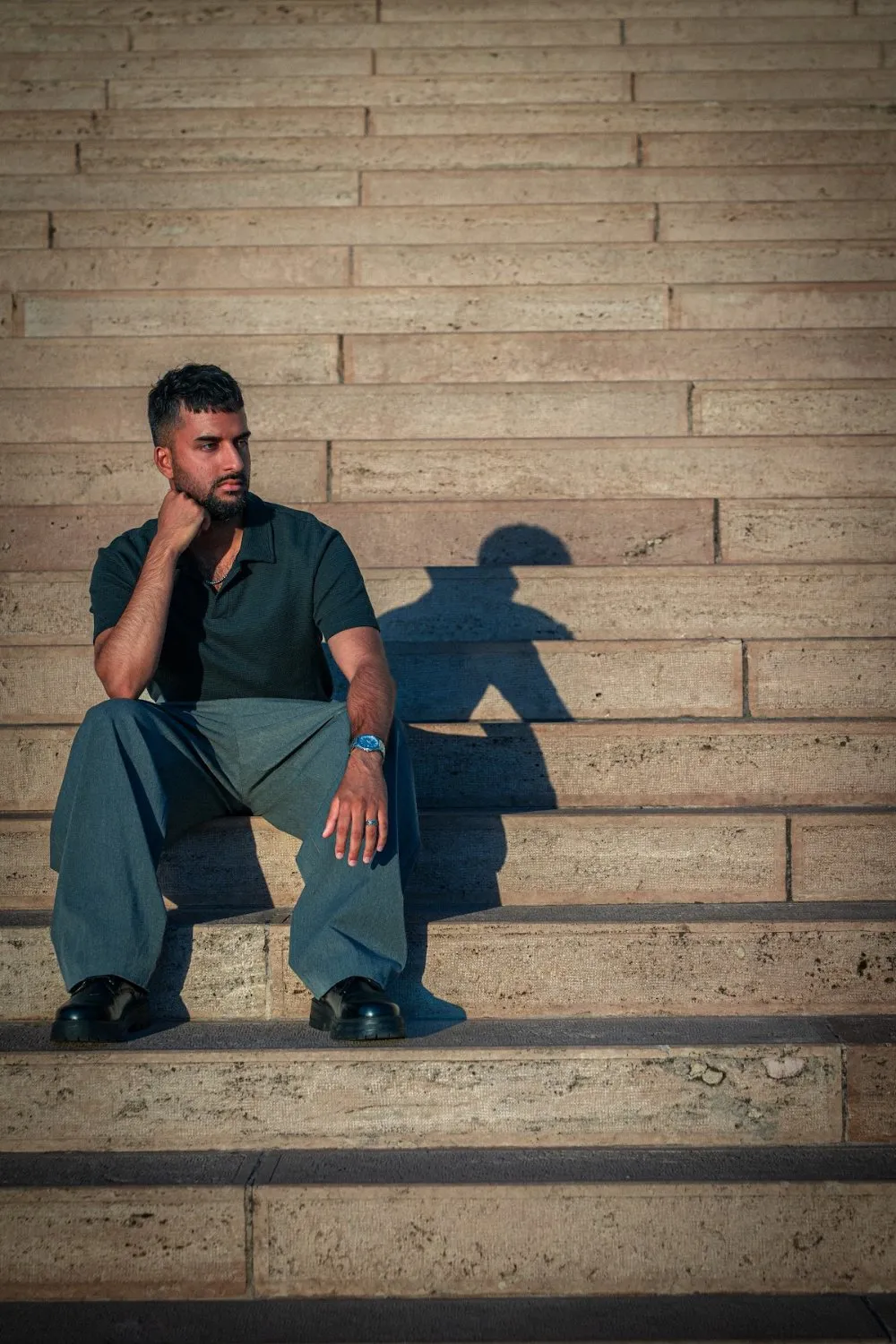 Model Zoubi seated on sunlit stone steps casting a long shadow, Parliament Gold editorial