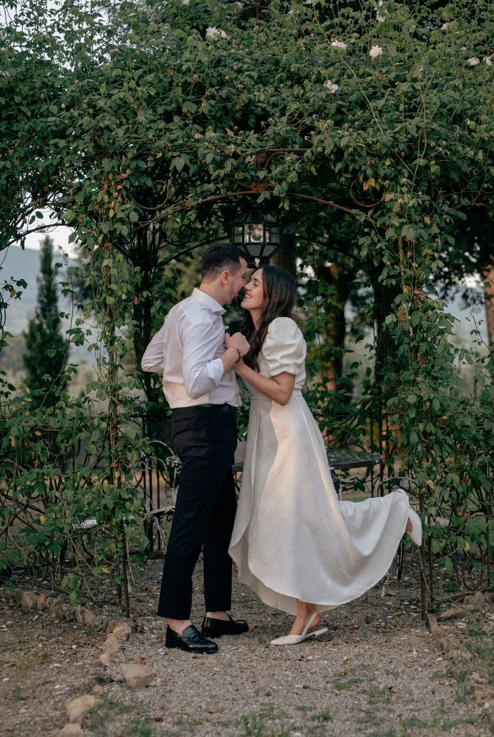 Couple embracing beneath a garden arbor as her dress swirls, Villa Dianella wedding photography by GROOVE Media