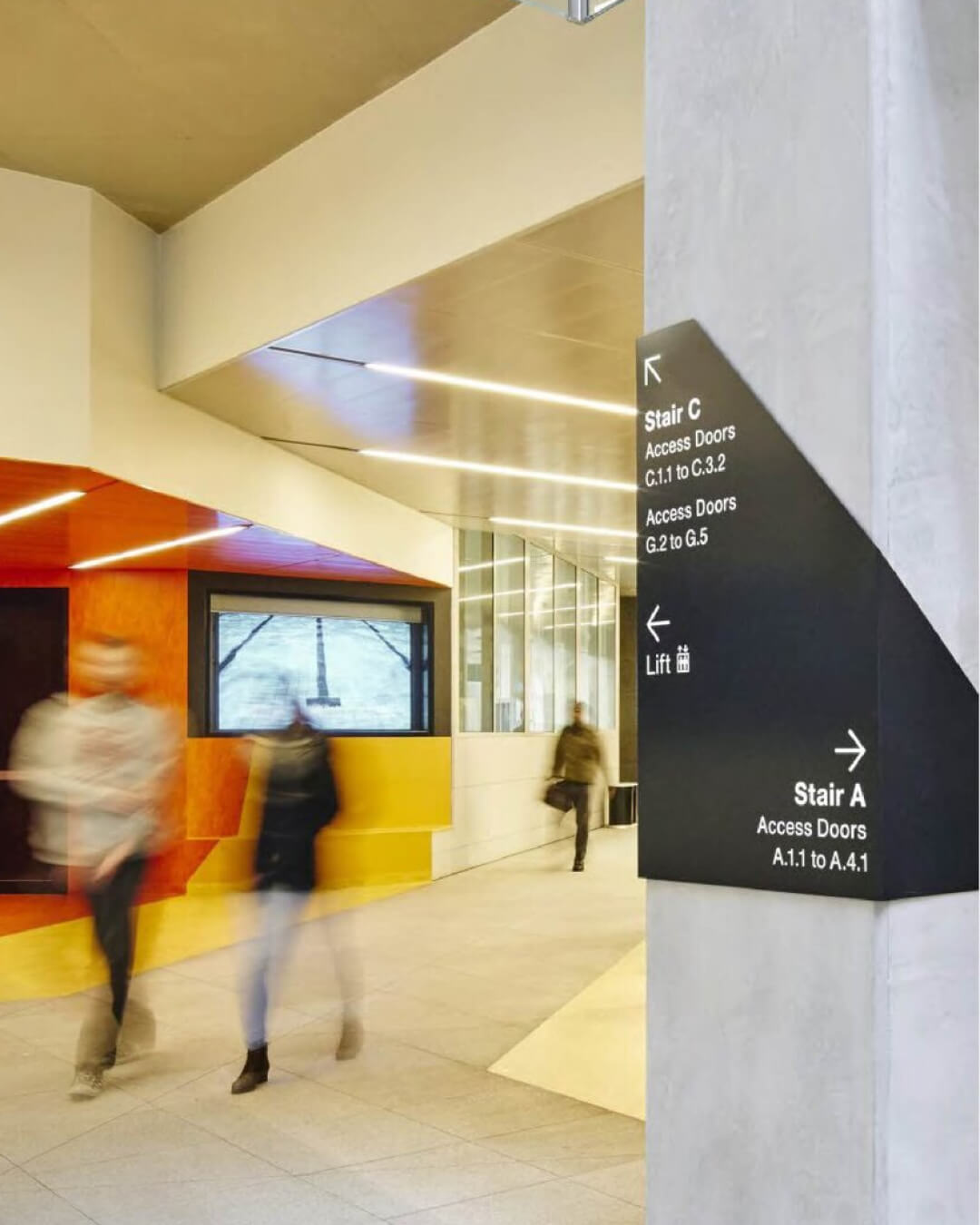 Indoor modern hallway with blurred people walking and a black directional sign on a pillar.