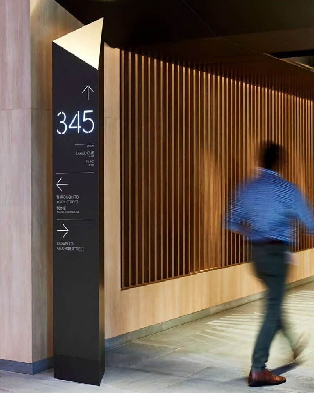 Tall black wayfinding sign with arrows and numbers 3, 4, 5 in a modern hallway with wood paneling.