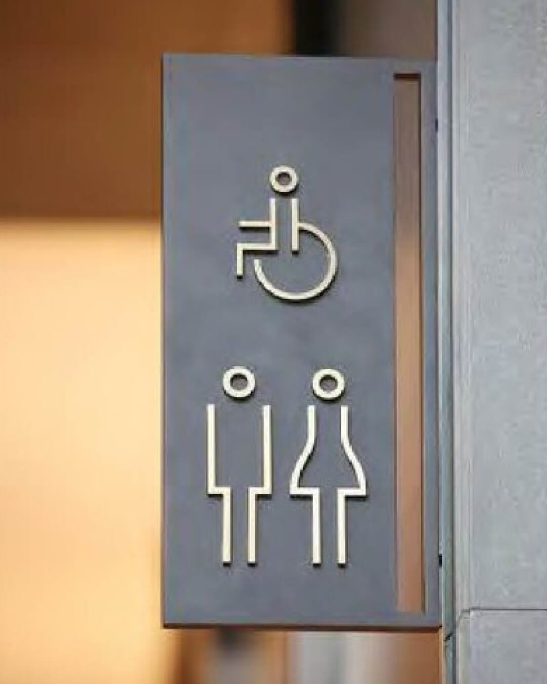 Gray restroom sign showing icons for wheelchair accessible, male, and female restrooms.