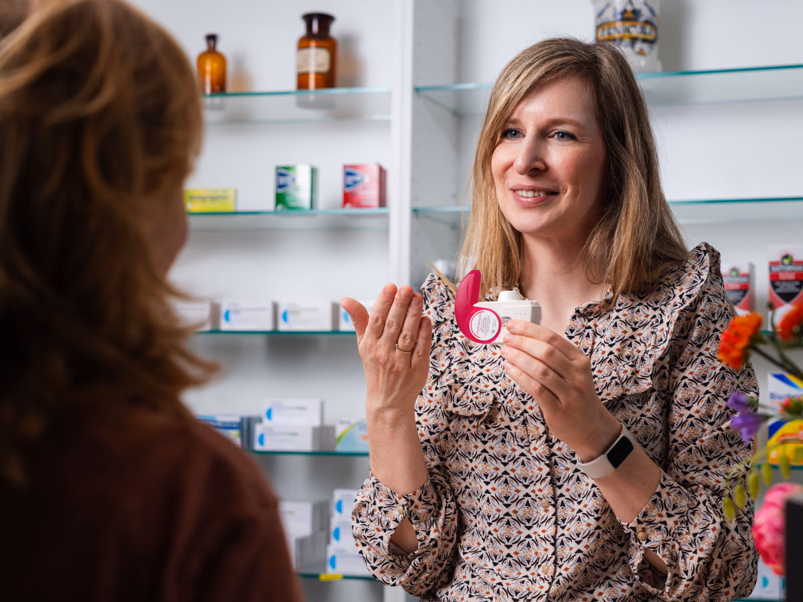 Apothekerin geeft persoonlijk advies aan klant en toont medicijnverpakking in apotheek.