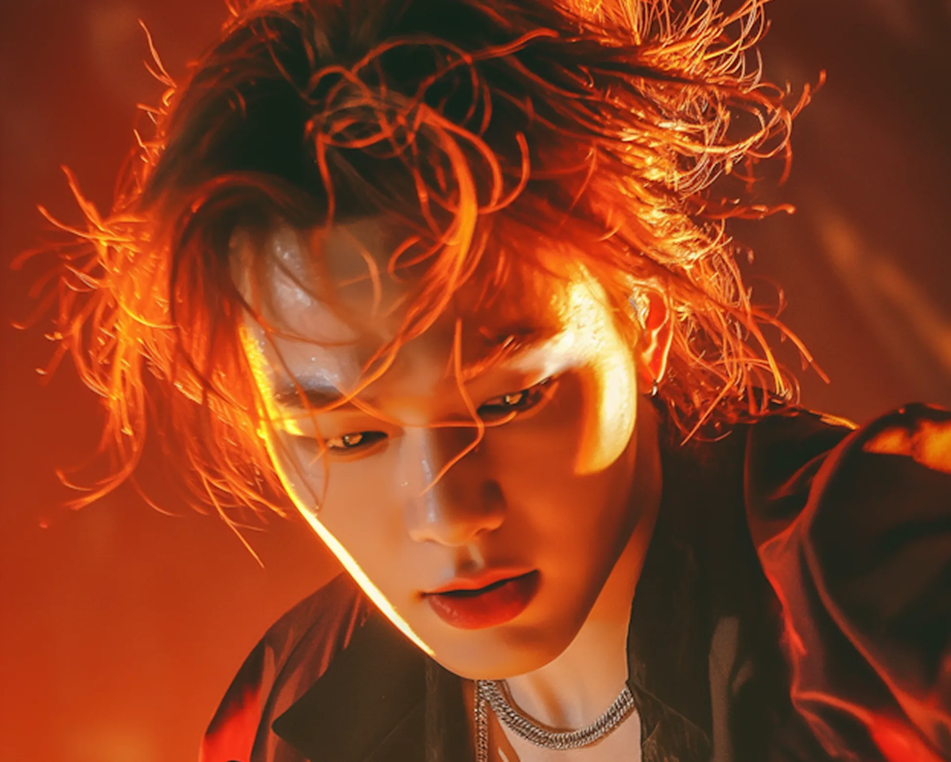 Close-up of a person with red hair illuminated by warm orange light, wearing a chain necklace and dark clothes.