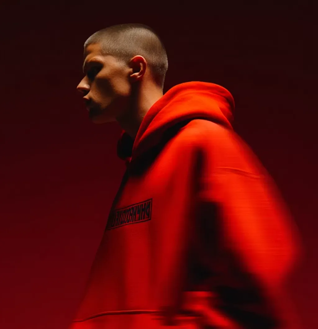 Profile of a person with short hair wearing a bright red hoodie against a dark red background.