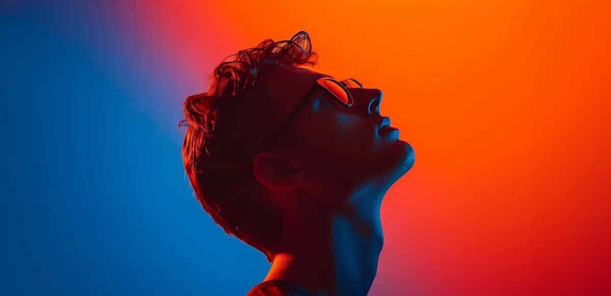 Side profile of a person wearing sunglasses with a colorful blue and orange gradient background.