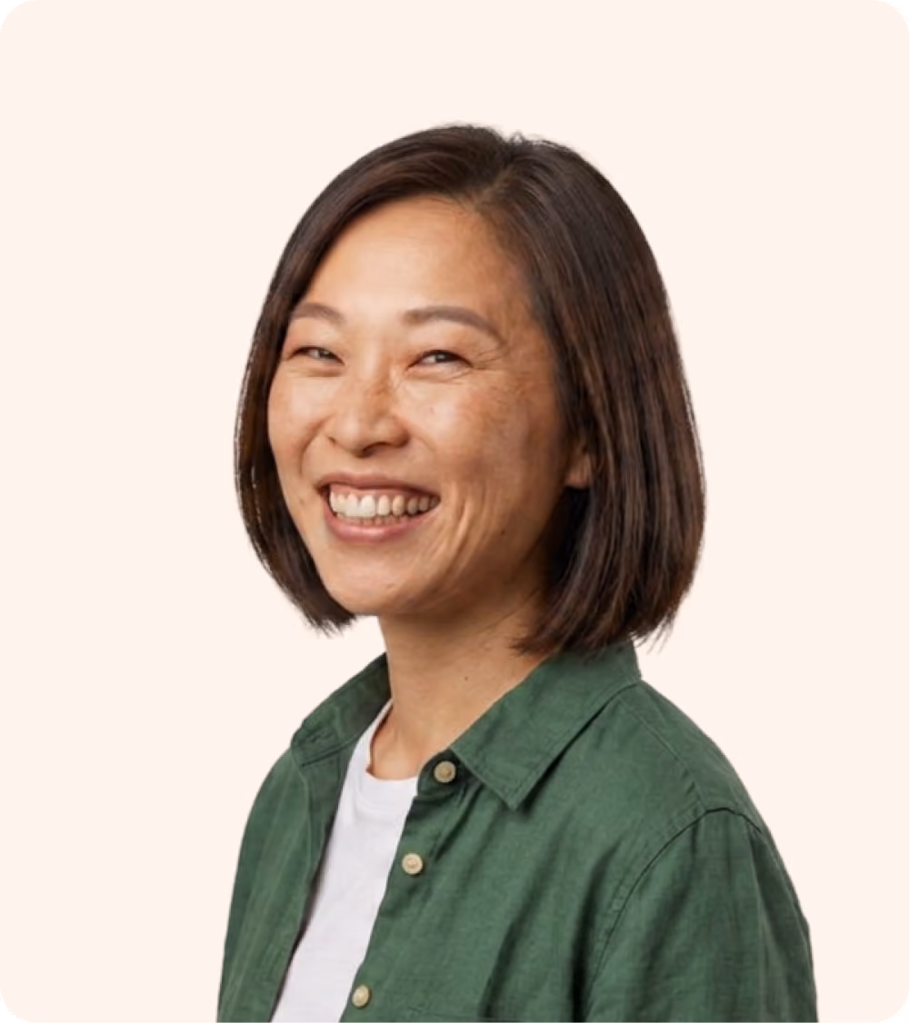 Smiling woman with short dark hair wearing a green shirt and white top on a light background.