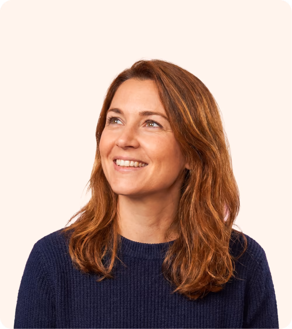 Smiling RevOps partner with shoulder-length auburn hair wearing a navy blue sweater, looking upwards.