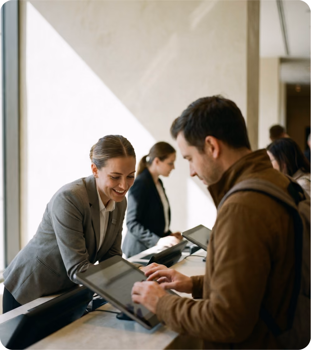 Hotel front desk staff assisting guests using touchscreen devices in a modern lobby.