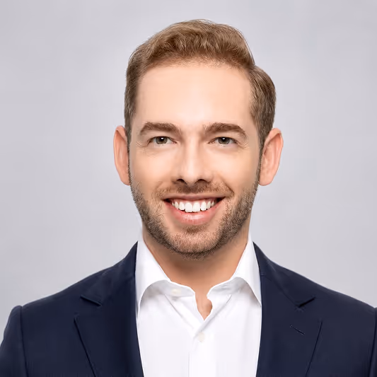 Smiling man with short light brown hair, trimmed beard, wearing white shirt and navy suit jacket.