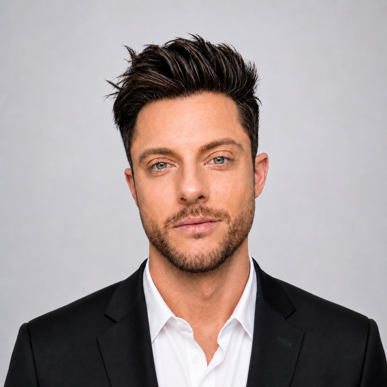 Portrait of a man with styled dark hair, light beard, wearing a white shirt and black blazer.