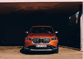 Front view of an orange BMW SUV parked in a shadowed garage.