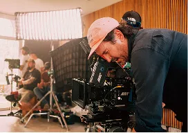Cameraman with a cap operating a professional video camera in an indoor studio setting.