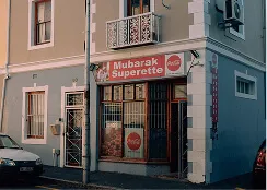 Corner store named Mubarak Superette with red signage and images of food items on the window.