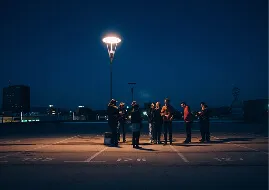 Group of people standing and talking under a streetlamp at night on an empty street.