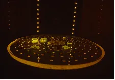 Circular board game with small yellow tokens placed on a dark background lit by vertical lines of small lights.