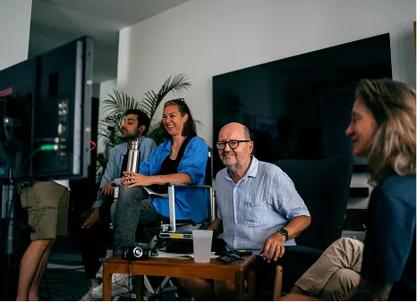 Four people sitting and smiling in a room with a large TV and a camera setup.
