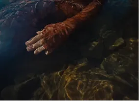 Hands of a person submerged partially in water with visible rocks and light reflections.