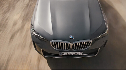Top view of a dark gray BMW car driving on a sandy, blurred road surface.