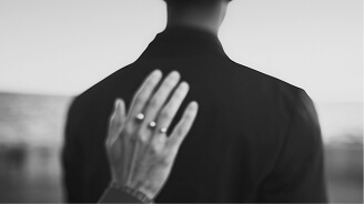 Hand with rings resting gently on the back of a person wearing a dark coat.