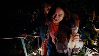 Young woman smiling and holding bottled drinks while standing outside at night.